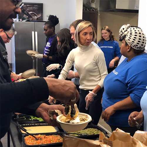 ボランティアはコミュニティキッチンで食べ物を提供しています。白いセーターを着た女性は、食べ物がメッキされて配られているので、他の人を導くのを助けます。